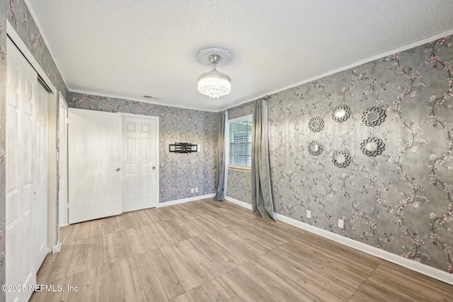 7437 Ortega Hills Dr, Jacksonville, FL 32244 - empty room featuring wood finished floors, wallpapered walls, crown molding, a textured ceiling, and baseboards