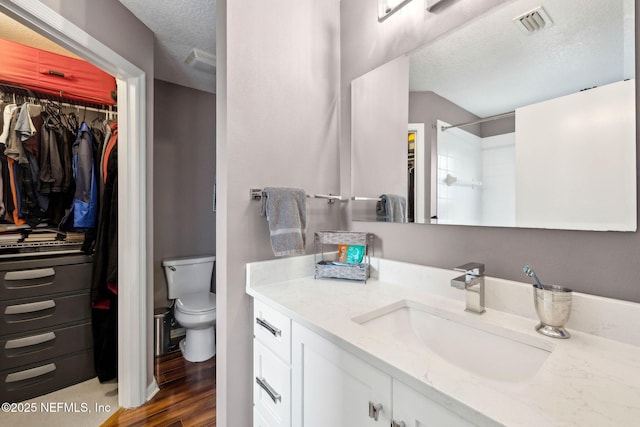 bathroom featuring a walk in closet, a textured ceiling, visible vents, wood finished floors, and vanity