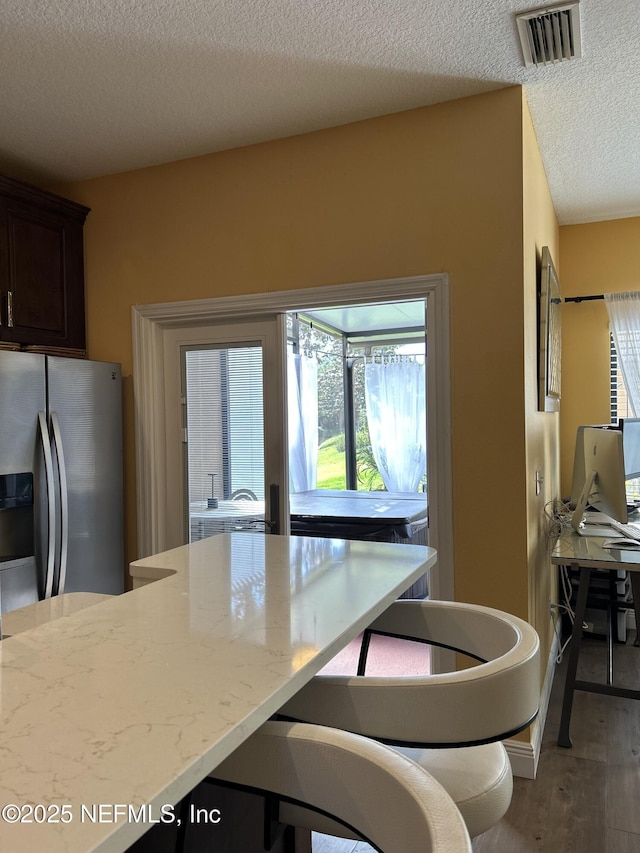 kitchen featuring visible vents, dark brown cabinets, stainless steel refrigerator with ice dispenser, a textured ceiling, and light wood finished floors