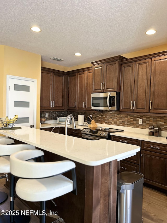 kitchen with appliances with stainless steel finishes, a breakfast bar area, backsplash, and dark brown cabinets