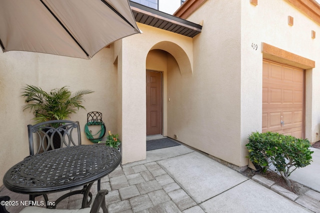 doorway to property with a patio, a garage, and stucco siding