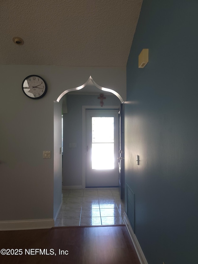 hall with arched walkways, a textured ceiling, light tile patterned flooring, and baseboards