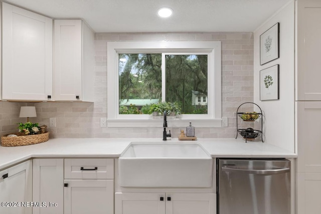 kitchen featuring stainless steel dishwasher, light countertops, white cabinets, tasteful backsplash, and a sink