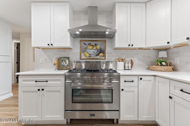 kitchen with backsplash, stainless steel gas range oven, light countertops, white cabinets, and wall chimney exhaust hood