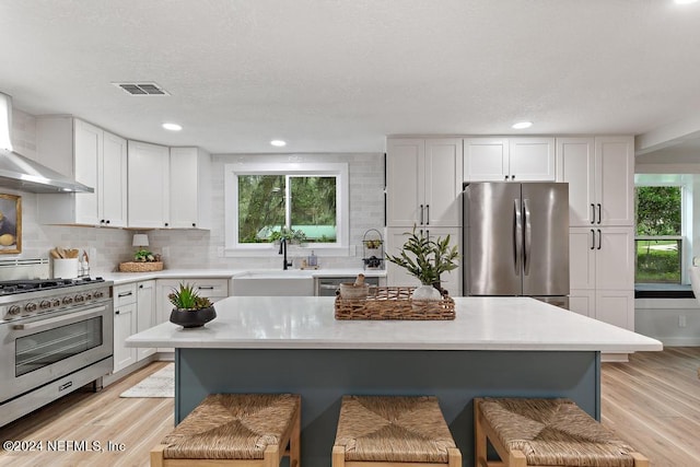 kitchen with wall chimney range hood, a kitchen breakfast bar, appliances with stainless steel finishes, and a sink