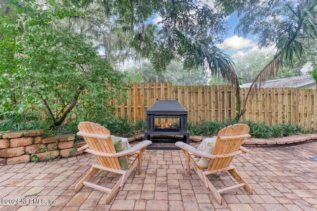 view of patio featuring fence and a lit fireplace