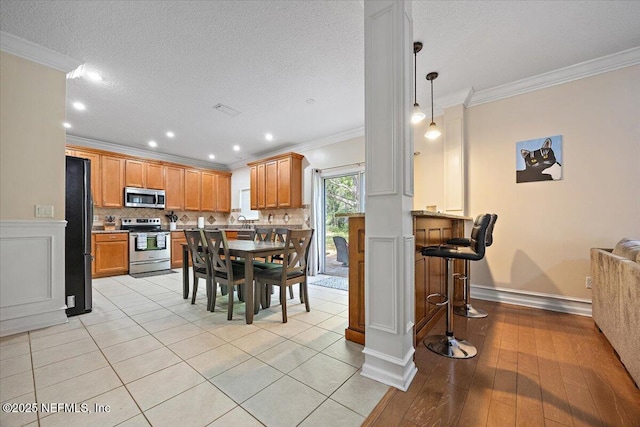 dining area featuring decorative columns, a textured ceiling, light wood-style floors, ornamental molding, and recessed lighting