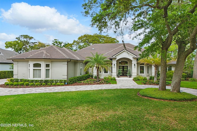 view of front of home featuring a tiled roof, french doors, a front yard, and stucco siding