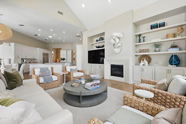 living room featuring light wood finished floors, built in shelves, recessed lighting, lofted ceiling, and visible vents