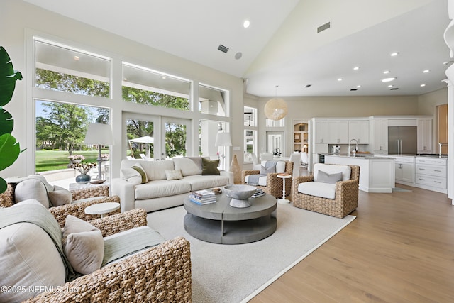 living room with high vaulted ceiling, visible vents, a wealth of natural light, and light wood-style floors