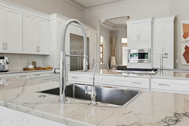 kitchen with ornamental molding, white cabinetry, stainless steel microwave, tasteful backsplash, and light stone counters