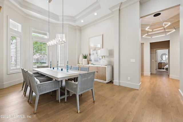 dining room with a raised ceiling, a chandelier, light wood-type flooring, a towering ceiling, and ornamental molding