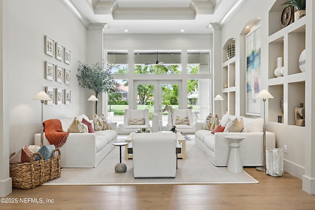 living area with ornamental molding, built in features, a towering ceiling, wood finished floors, and french doors