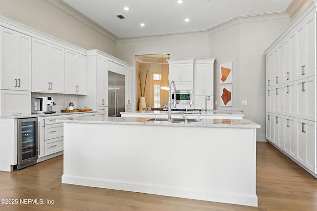 kitchen featuring a kitchen island with sink, crown molding, a sink, wine cooler, and recessed lighting