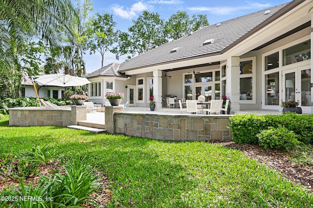 rear view of property with ceiling fan, a patio, stucco siding, a yard, and a tile roof
