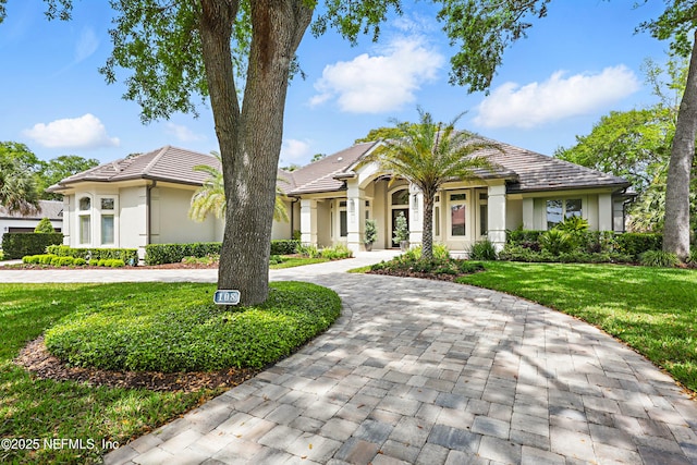 view of front facade featuring curved driveway, a front lawn, stucco siding, and a tile roof