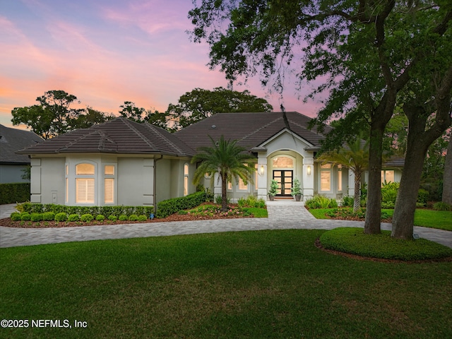 ranch-style home featuring french doors, stucco siding, a tiled roof, and a front lawn