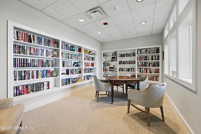 sitting room with carpet flooring, bookshelves, built in features, baseboards, and visible vents