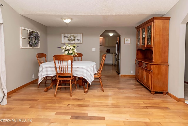 dining room featuring arched walkways, baseboards, and light wood-style flooring