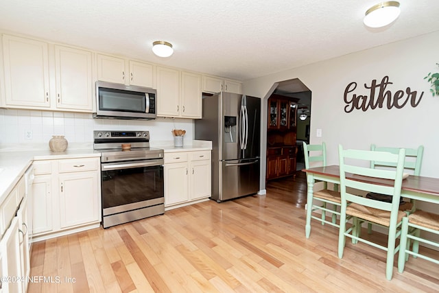 kitchen featuring light countertops, appliances with stainless steel finishes, arched walkways, and light wood-style flooring