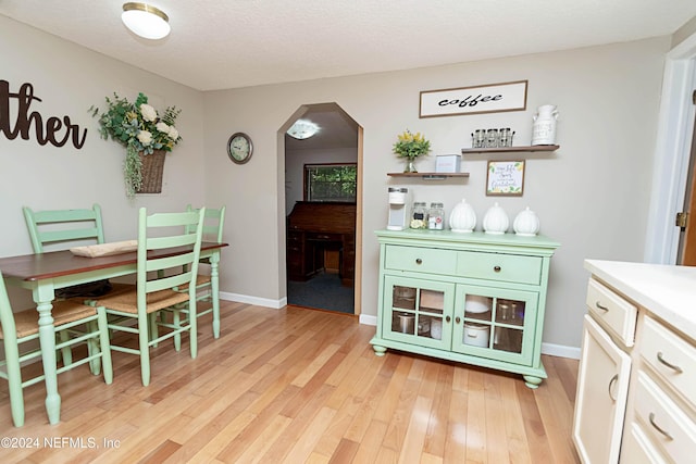 dining space featuring arched walkways, baseboards, and light wood-style flooring