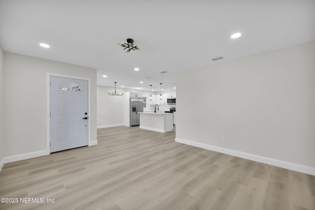unfurnished living room featuring a notable chandelier, visible vents, a sink, and light wood-style floors