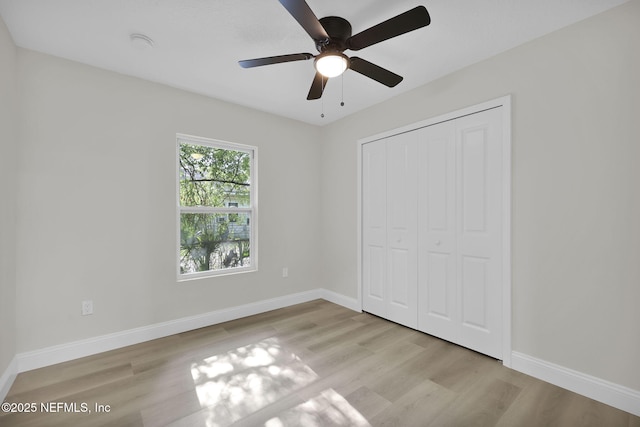 unfurnished bedroom featuring baseboards, a ceiling fan, wood finished floors, and a closet