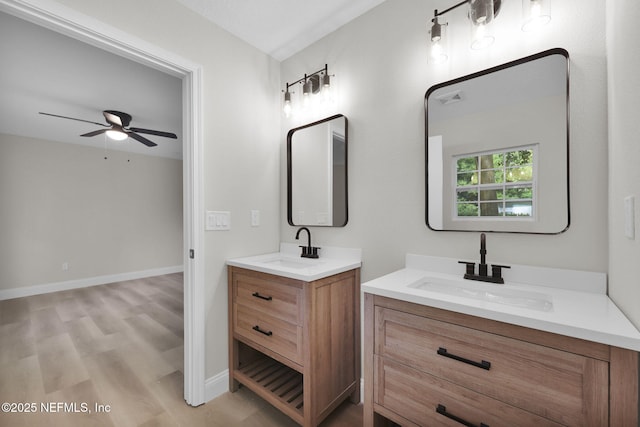 full bath featuring wood finished floors, a sink, ceiling fan, and two vanities