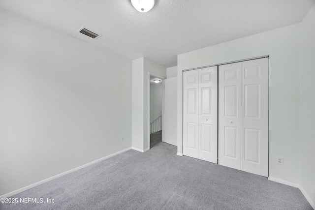 unfurnished bedroom with carpet floors, a textured ceiling, baseboards, visible vents, and a closet