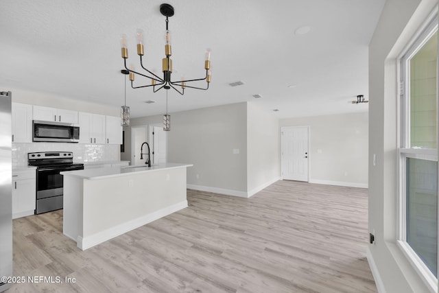 kitchen featuring light countertops, an inviting chandelier, stainless steel appliances, white cabinetry, and an island with sink