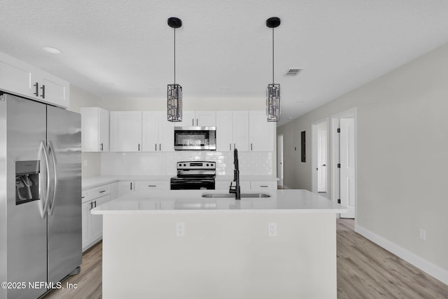 kitchen featuring a kitchen island with sink, backsplash, white cabinets, light wood-style floors, and stainless steel appliances
