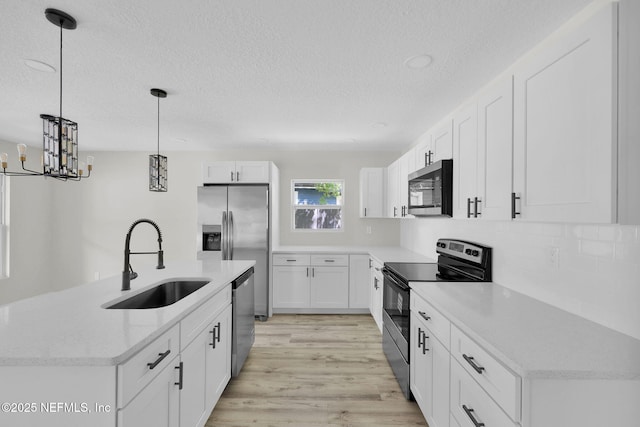kitchen with white cabinets, appliances with stainless steel finishes, a sink, a textured ceiling, and light wood-type flooring