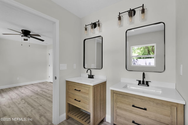 full bathroom featuring wood finished floors, a sink, a ceiling fan, and two vanities