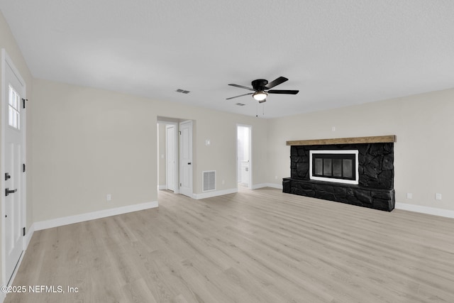 unfurnished living room featuring a ceiling fan, visible vents, a stone fireplace, and light wood finished floors
