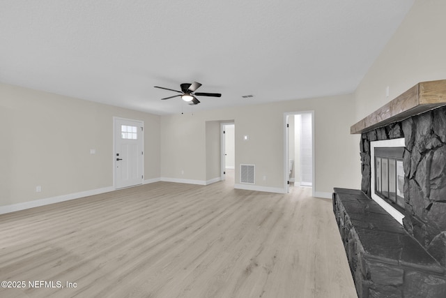 unfurnished living room with ceiling fan, a stone fireplace, light wood-style flooring, baseboards, and visible vents