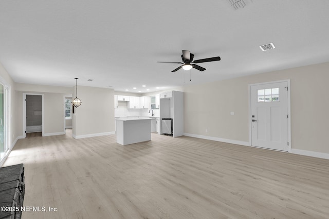 unfurnished living room featuring baseboards, a ceiling fan, light wood-type flooring, and visible vents