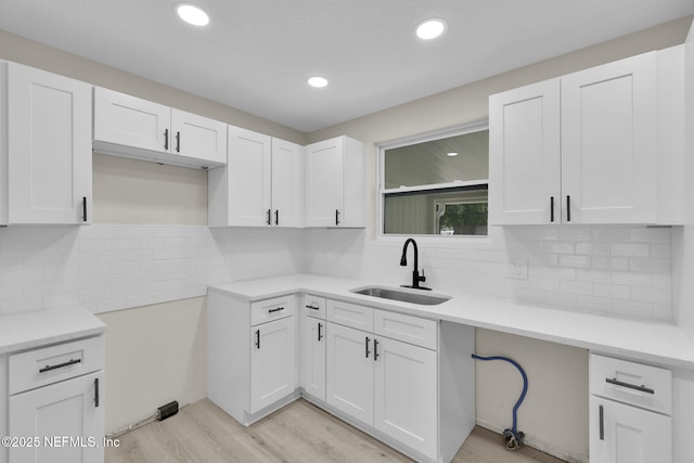 kitchen featuring a sink, white cabinets, light wood-type flooring, and tasteful backsplash