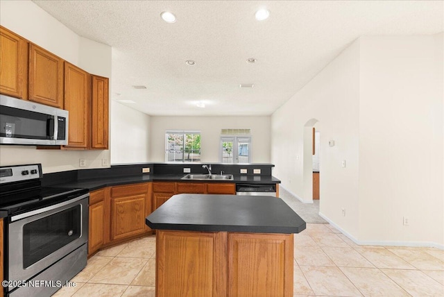 kitchen with a peninsula, dark countertops, appliances with stainless steel finishes, and a sink