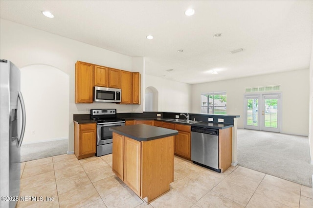 kitchen with dark countertops, arched walkways, a sink, light carpet, and stainless steel appliances
