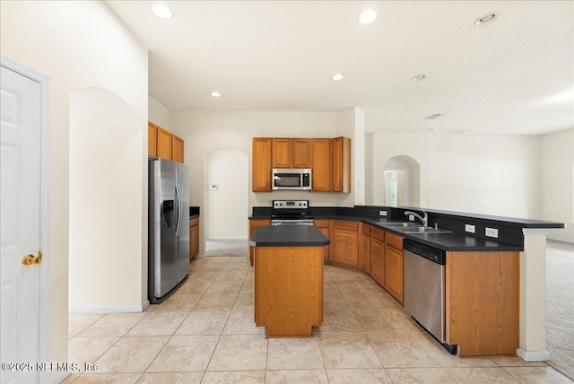 kitchen featuring dark countertops, a sink, arched walkways, a center island, and stainless steel appliances