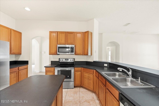 kitchen featuring a sink, dark countertops, brown cabinets, arched walkways, and stainless steel appliances