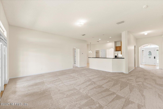 unfurnished living room featuring arched walkways, baseboards, and light colored carpet