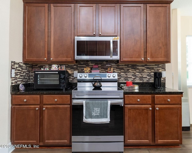 kitchen featuring a toaster, appliances with stainless steel finishes, tasteful backsplash, and dark stone countertops