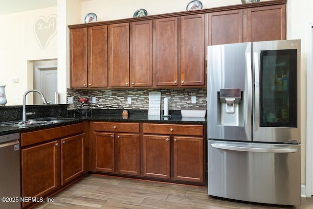 kitchen featuring a sink, light wood finished floors, dark stone countertops, stainless steel appliances, and backsplash