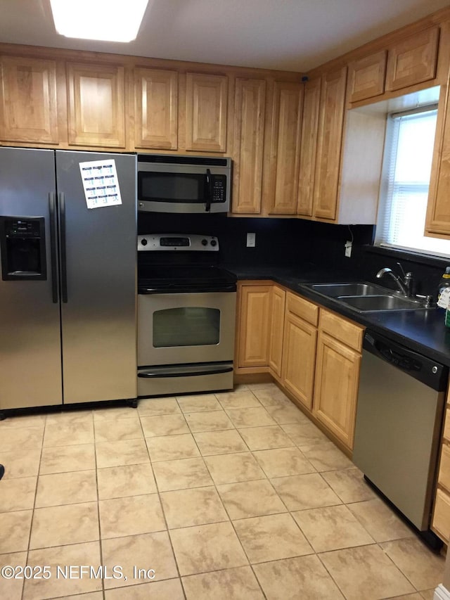 kitchen with light brown cabinetry, light tile patterned flooring, dark countertops, a sink, and stainless steel appliances