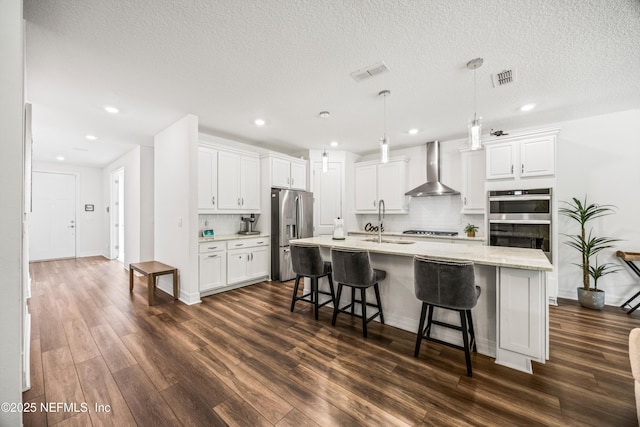 kitchen featuring appliances with stainless steel finishes, dark wood-style floors, a sink, and wall chimney exhaust hood