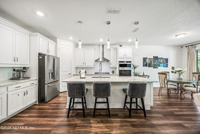 kitchen featuring a breakfast bar area, visible vents, tasteful backsplash, stainless steel appliances, and wall chimney exhaust hood