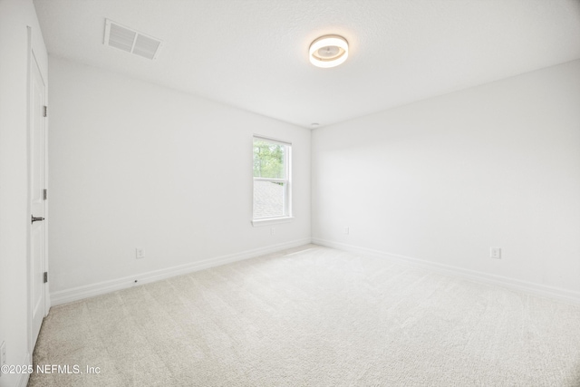 spare room featuring visible vents, baseboards, and light colored carpet
