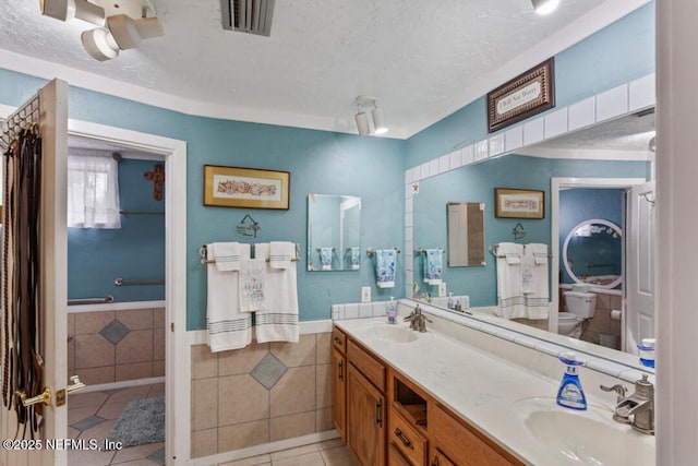 full bathroom featuring toilet, tile patterned floors, tile walls, and a sink