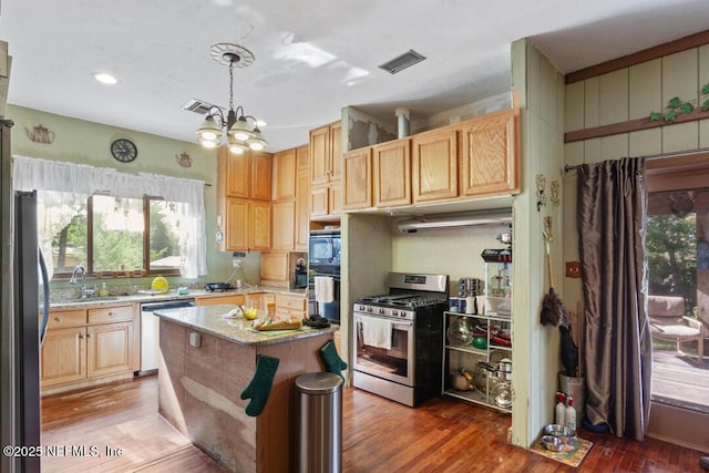kitchen featuring visible vents, appliances with stainless steel finishes, wood finished floors, light stone counters, and a notable chandelier